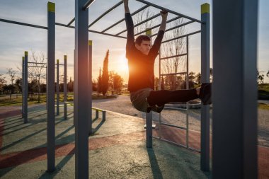 Genç atletik adam spor yapıyor spor yapıyor ve gün batımında karın kasları için halka bacağı kaldırıyor. Spor salonunda kaslar, vücut geliştirme ve dayanıklılık eğitimi. Yüksek kalite fotoğraf