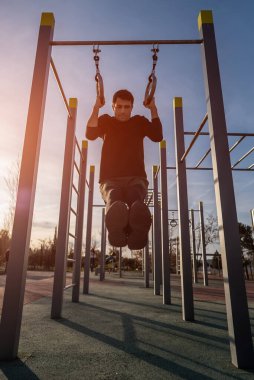 Spor salonunda yüzüklerini çalıştıran genç bir atletik gün batımında sokak spor salonunda barfiks çekiyor, vücut geliştirme ve dayanıklılık eğitimi kavramı. Yüksek kalite fotoğraf