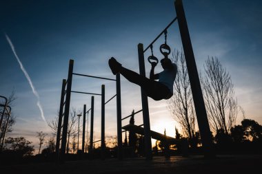 Genç atletik adam spor yapıyor spor yapıyor ve gün batımında karın kasları için halka bacağı kaldırıyor. Spor salonunda kaslar, vücut geliştirme ve dayanıklılık eğitimi. Yüksek kalite fotoğraf