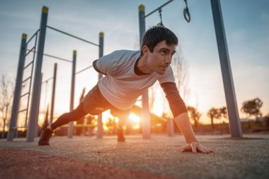 Genç atletik adam spor yapıyor ve gün batımında sokak spor salonunda tahtada duruyor. Vücut geliştirme ve dayanıklılık eğitimi kavramı. Yüksek kalite fotoğraf