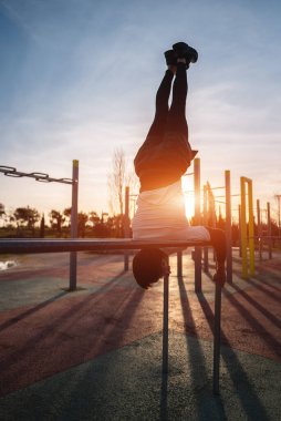 Spor salonunda spor yapan genç sporcu gün batımında paralel barlarda amuda kalkarak vücut geliştirme ve dayanıklılık eğitimi alıyor. Yüksek kalite fotoğraf