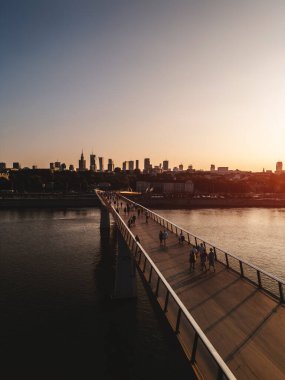Günbatımında Vistula nehri üzerinde yeni inşa edilmiş yaya ve bisiklet modern köprüsü, şehir merkezindeki finans bölgesi ve Varşova şehrinin modern mimarisi, gökyüzü manzarası 4k. Yüksek kalite fotoğraf