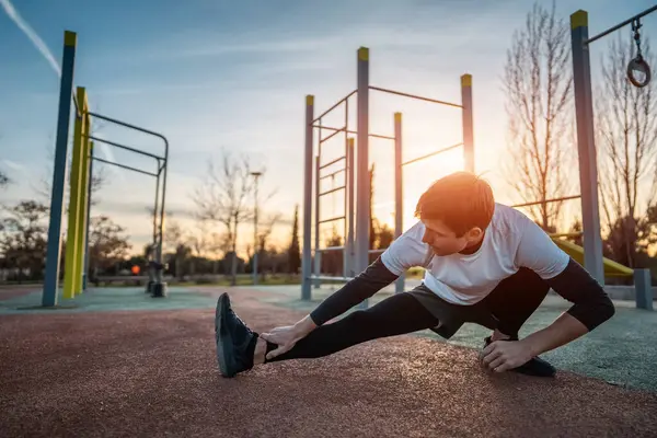 Genç atletik adam spor salonunda egzersiz yapıyor ve gün batımında sokak spor salonunda bacaklarını esnetiyor, vücut geliştirme ve dayanıklılık eğitimi kavramı. Yüksek kalite fotoğraf