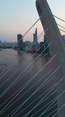 Saigon nehri üzerinde aydınlatma ışıkları olan modern kablolu köprü, arka planda finans merkezi, Ho Chi Minh şehri, Vietnam hava manzaralı. Yüksek kalite 4k görüntü, dikey video