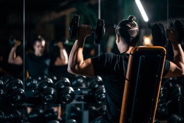 Erkek vücut geliştirici spor salonunda omuzları için dambıl presi yapıyor, antreman sırasında halterli deltoid kasları çalıştırıyor. Yüksek kalite fotoğraf