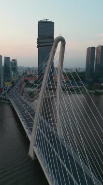 Saigon nehri üzerinde aydınlatma ışıkları olan modern kablolu köprü, arka planda finans merkezi, Ho Chi Minh şehri, Vietnam hava manzaralı. Yüksek kalite 4k görüntü, dikey video