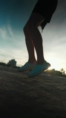 Gün batımı egzersizi sırasında deniz kıyısında ip atlayan vücut geliştiriciyi, güneş batarken okyanus kıyısında atlama halatıyla antrenman yapan sporcuları kardiyo egzersizi için dikey video 4k çekimleri. Yüksek kalite 4k görüntü