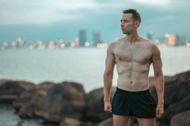 Kaya üzerindeki atlet güç ve doğa mücadelesi sergiliyor, dağ zirvesindeki kaslı atletizm sporcusu zindelik ve engebeli başarı yayıyor. Yüksek kalite fotoğraf