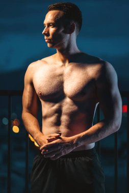 Geceleri güçlü poz veren kaslı bir sporcu, dayanıklılık ve adanmışlık, akşam siluetinde güç ve disiplin sergileyen mükemmel vücutlu bir adam. Yüksek kalite fotoğraf