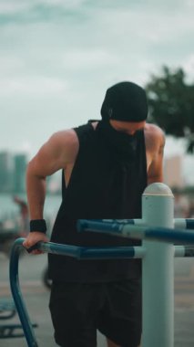 Erkek vücut geliştirici gün batımında paralel barlarda dalış yapıyor, Sporcu adam gün batımında açık hava ekipmanlarıyla trisepsleri eğitiyor. Yüksek kalite 4k görüntü, dikey video