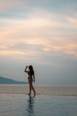 Güneşin doğuşunda havuz kenarında yürüyen güzel bir kız, sakin bir zarafet ve sabah barışı, gün batımında ya da gün doğumunda okyanus kenarında gezinen çarpıcı bir kadın. Yüksek kalite fotoğraf