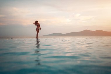 Güneşin doğuşunda havuz kenarında yürüyen güzel bir kız, sakin bir zarafet ve sabah barışı, gün batımında ya da gün doğumunda okyanus kenarında gezinen çarpıcı bir kadın. Yüksek kalite fotoğraf