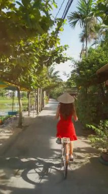 Vietnam köyünde geleneksel şapkasız bisiklet süren kız, kırsal Vietnam köyünde bisiklet süren kadın doğa yolculuğunu ve yerel geleneği ön plana çıkarıyor, 4k dikey video. Yüksek kaliteli görüntüler