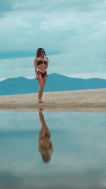 Güneşin doğuşunda deniz kıyısında yürüyen güzel bir kız, sakin bir zarafet ve sabah barışı, gün batımında okyanus kenarında gezinen çarpıcı bir kadın, dikey video. Yüksek kaliteli FullHD görüntüler