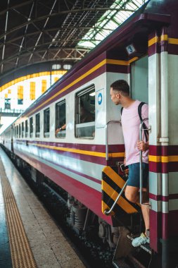 Seyyah adam tren istasyonunda trene biniyor. Sırt çantalı genç adam tren peronunda yolculuğa başlıyor. Yüksek kalite fotoğraf