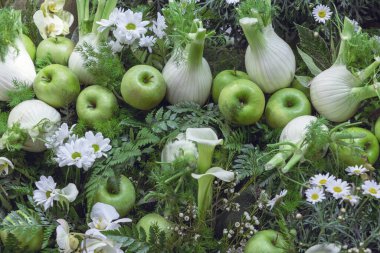 Closeup assortment of freshly picked vegetable fennel bulbs and green apples decorated with flowers for sale at local farmers market. Veganuary and healthy vegan organic food concept. Harvest festival