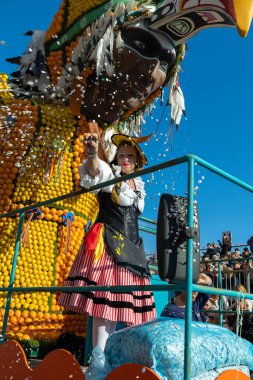 Menton, France-February 12, 2023: Woman dressed colorful carnival costume throwing confetti during carnival parade of Lemon Festival.