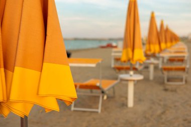 Seçici bir odak noktası ve kapalı güneş şezlongları ve deniz sahilinde insan olmadan kapalı şemsiyeler. Tatil kavramı.