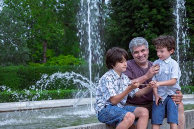 Babam ve iki oğlum çeşmelerin yanındaki parkta dinleniyorlar. Ailene iyi eğlenceler. Samimi insanlar. Yaşam tarzı. Komik bir an. Sıcak bir yazın havası. Samimi insanlar. Babalar günün kutlu olsun..