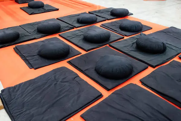 Black meditation cushions and mats neatly arranged on a bright orange floor. Yoga or meditation hall for promotes relaxation and focus. Concept meditation practice,Spiritual or personal growth.