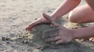 Güneşli bir plajda kum kalıpları dökerken, bir çocuğun ellerine yakın çekim yapmak, neşeli bir yaratıcılık anı yakalamak ve çocukluğun basit zevklerini yakalamak. Tatil kavramı..