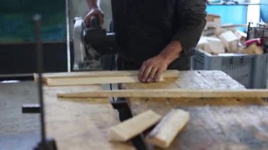 Seçici odaklanma ve atölyede çalışan bir marangozun yakın çekimi. Marangoz tahta blokları ve tahta tahtaları testereyle keser. İşçi Bayramı.