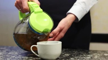 Yakın plan kadın elleri, cam çaydanlıktan siyah mermer bir masanın üzerindeki beyaz fincana çay döker. Uluslararası Çay Günü.
