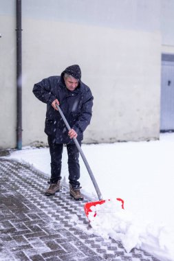 Seçici odak adam kış mevsiminde kırmızı kürekle garaj yolunda kar kürüyor. Dünya Karlı Günü. Kar fırtınası, doğal afetler ve kar yağışı