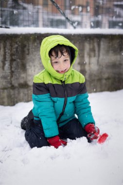 Renkli kışlık ceketli çocuk karla kaplı bahçede neşeyle oynuyor. Dünya Karlı Günü.