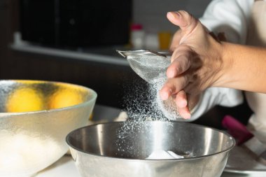 Pişirme hazırlığı için dişi ellerinin unu kaseye ellediği yakın plan. Turta pişirme aşaması