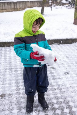 Yeşil ceketli çocuk kış harikalar diyarında kar tutuyor. Dünya Karlı Günü.