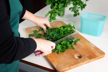 Tahtada taze maydanoz, mutfak hazırlığı için bıçakla doğranıyor. Maydanozu kış deposuna hazırlıyorum.