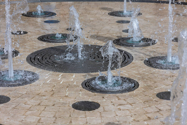 Interactive circular water fountain with bubbling jets on paved surface.