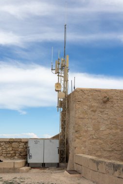 Alicante, İspanya - 9 Mart 2025: Taş yapı üzerinde mavi gökyüzüne karşı iletişim antenleri.