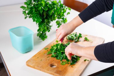 Mutfakta ahşap bir kesme tahtasının üzerinde maydanoz doğrayan birinin yakın çekimi. Sağlıklı yemek hazırlama ve ev yapımı yemekler..