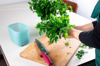 Kadın mutfak masasında taze maydanoz, ev yemeği ve sağlıklı yiyecek konsepti hazırlıyor. Maydanozu kış deposuna hazırlıyorum..