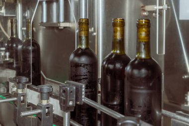 Modern bir şaraphanenin üretim hattındaki şarap şişeleri endüstriyel çevredeki otomatik şişeleme sürecini gösteriyor.