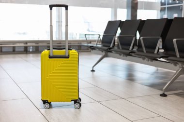 Parlak sarı bavul havaalanı terminallerinde tek başına bekliyor. Etrafı boş koltuklarla çevrili. Seyahat, tatil ve heyecan verici yolculukları çağrıştırıyor.
