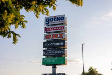 Piacenza, İtalya - 11 Mayıs 2025: İtalya 'daki Gotico alışveriş merkezinde açık bir gökyüzünün altında bulunan süpermarket ve giyim mağazası da dahil olmak üzere çeşitli perakende markalarının logolarının yer aldığı büyük sütun işareti