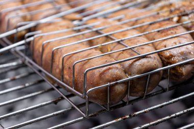 Sıcak kömürlerin üzerinde metal bir sepetin içinde ızgara yapan sulu sosisleri kapatın, havayı ağız sulandırıcı aromalarla doldurun ve yaz toplantıları için mükemmel bir barbekü atmosferi yaratın.