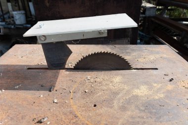 Tahtayı kesen dairesel testere bıçağını kapat, ahşap atölyesinde paslı bir metal masa üzerinde talaş ve enkaz oluştur, marangozluğun alet ve işlevlerini vurgula