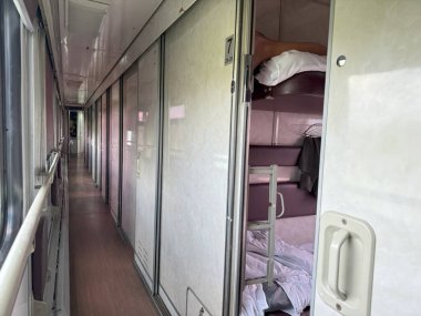 Boş bir tren vagonu koridoru yolcu kompartımanlarının sürgülü kapılarını, ranza, battaniye ve yastıkları gösteriyor.