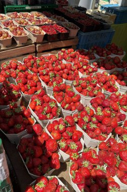 Renkli bektaşi üzümü ve frenk üzümü ile çevrili, bir çiftçi pazarındaki bir masada sergilenen olgun kırmızı çilekler, canlı bir sahne yaratır.