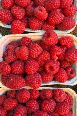 Karton böğürtlenler olgun, canlı kırmızı ahududularla dolup taşarak bir çiftçi pazarında renkli ve cezbedici bir görüntü yaratarak taze ve yerel kaynaklı ürünlerin bolluğunu gözler önüne seriyor.