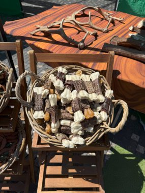 Hasır sepet, arka planda boynuzları sergilenen bir açık pazarda, muhtemelen doğal malzemelerden yapılmış köpek maması çeşitleriyle dolu ahşap bir tezgahta duruyor.