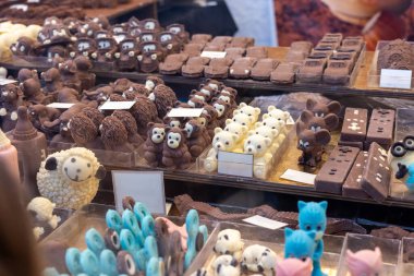 Çeşitli hayvan ve nesnelere benzeyen çikolata figürleri bir market tezgahındaki raflarda düzgün bir şekilde düzenlenerek potansiyel müşteriler için görsel olarak çekici bir görüntü oluşturuluyor.