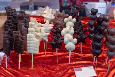 Kalp, yıldız, pençe ve çikolata şeklinde çeşitli çikolata lolipopları bir markette çubuklarda sergilenerek tatlı ve cezbedici bir ikram yaratılıyor.