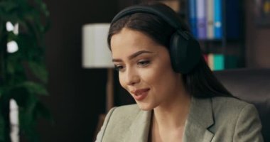 Sakin, güzel bir kadın, online konferanstan sonra kablosuz kulaklıklarla masada rahatlıyor. .