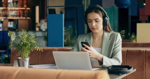 Young Woman Restaurant Listens Music Wearing Wireless Headphones Working Laptop — Video