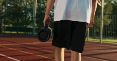 Spor giyim bölümündeki yakın plan fotoğrafçı portatif ses hoparlörü tutuyor. Aküyle çalışan hoparlör. Moda kıyafetleri içinde yakışıklı bir genç, arkadaşlarıyla basketbol oynayarak stadyuma gidiyor. .